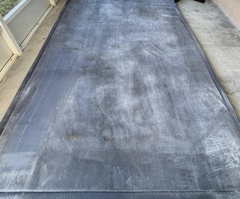 Dusty, soiled gray area rug on a screened patio before cleaning